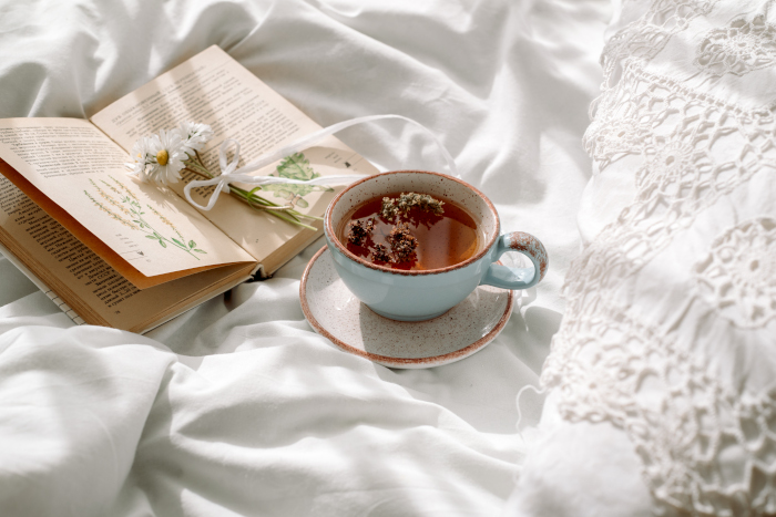 Openwork lace, cotton white blanket. book botany, mug with natural herbal tea made from mint, summer daisy flowers. Morning breakfast in bed. Provence and retro style. Clean cosiness and freshness.